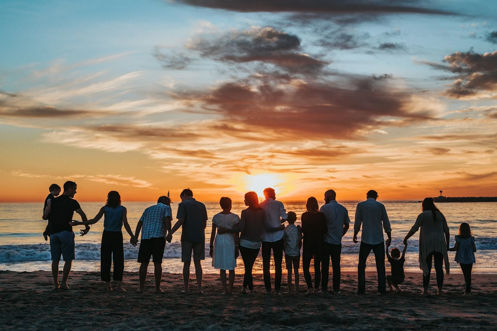A family holding hands by the water at sunset, viewed from behind